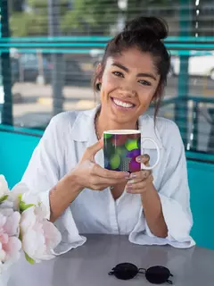 Mulher sorridente segurando uma caneca com design de bolas abstratas em um ambiente moderno.