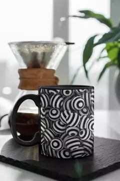 Caneca preta com design moderno de bolas abstratas em preto e branco, posicionada sobre uma superfície escura.