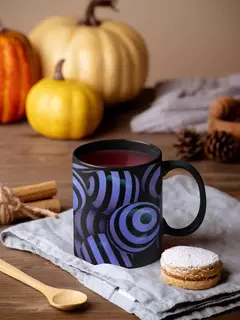 Caneca preta com design abstrato de bolas em azul e roxo, acompanhada de um biscoito e elementos de outono ao fundo.