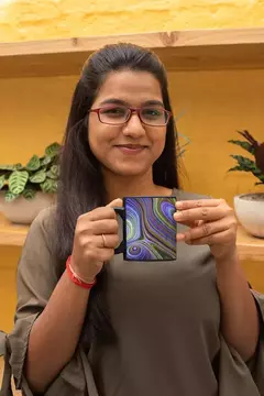 Mulher segurando uma caneca com design de bolas abstratas coloridas em fundo preto.