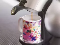 Caneca branca decorada com borboletas coloridas sendo preenchida com café.