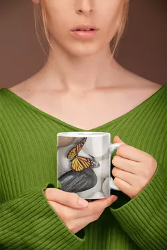 Caneca Borboletas MOD5 com uma borboleta amarela e preta sobre pedras, segurada por uma mulher vestindo um suéter verde.