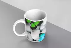 Caneca branca com borboletas verde e azul sobre pedras brancas.