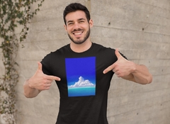 Homem sorrindo com uma camiseta preta exibindo uma ilustração de nuvens em um céu azul.