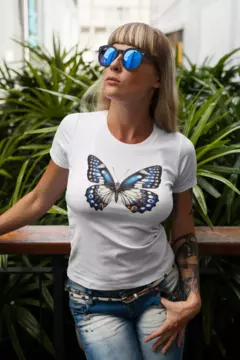 Camisa branca BabyLook com estampa de borboleta, modelo mod4, sendo usada por uma mulher com óculos escuros em um ambiente com plantas.