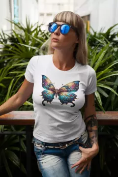 Modelo usando uma camisa branca BabyLook com estampa de borboleta colorida, em um ambiente com muitas plantas ao fundo.